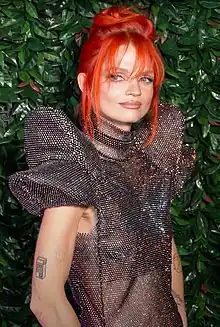 Medium shot of a red-haired woman, as she is looking away from the camera, wearing a silver top.