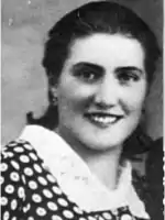 a black and white photo of a woman, maria occhipinti smiling at the viewer. she has dark, shoulder-length hair and a spotted blouse.