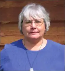 Portrait photograph of a woman before a clapboard building.