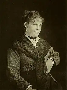 A black-and-white portrait of a young woman wearing a checkered dress and a shawl
