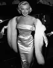 Photograph of a blonde woman wearing a glamorous dress, a fur scarf, and gloves