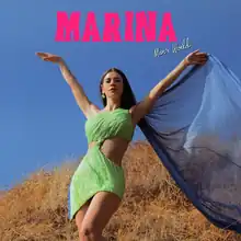 Welsh singer-songwriter Marina Diamandis appears in a sleeveless green dress that partially exposes the sides of her midriff; a blue cape flows in the wind behind her and she stands in a field with the sky in the background. The words "Marina", which was written in a capitalized and bright pink font, and "Man's World", which was written in a white cursive font, appear.
