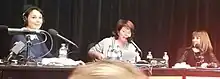 Three women with microphones before an audience