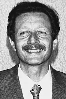 Close-up of Mario Rossi in his early forties, shortly after his release from the Red Brigades' kidnapping. A smiling face, with a mustache. He is wearing an elegant jacket, a white shirt, and a polka dot tie with a Windsor knot.