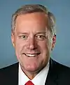 facial portrait of a smiling middle-aged man wearing a dark blue suit with a red tie