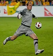 A man in a grey football kit in the act of kicking a ball.
