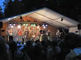 a group of men playing horns, guitars, and percussion in a tent