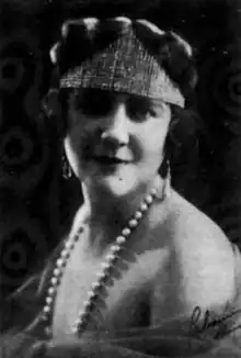 A white woman wearing a boxy hat and a strand of pearls with bare shoulders