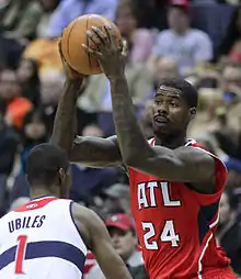 A man wearing a red jersey with the number 24 while holding a basketball.