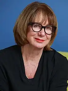 Mary-Louise McLaws, a white woman in her 60s with a brown bob haircut and black glasses, looks at the camera with a slight smile.