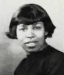 A young dark-skinned woman with dark hair cut in a short bob with bangs, wearing a dark turtleneck