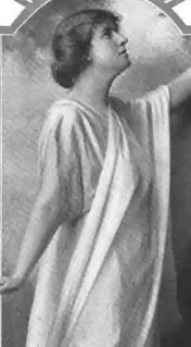 A white woman wearing a white draped cloth, in a dance pose with both arms extending out of the frame of the image.