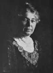 An older white woman wearing a dark dress with a white lace collar.