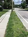 A curb strip in suburban Greater Boston, Massachusetts. Outside of rural areas in New England, devil strips are narrow – the one pictured is 52 inches (130 cm; 1.3 m) from curb to sidewalk.  They are usually not maintained by the municipality, but rather by the property owner, and are used primarily to provide space for utility poles.