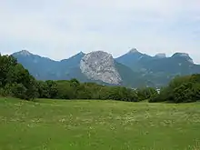 Sloping mountain rising over a meadow, above a valley, with other mountains in the background.