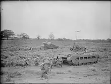 In the foreground, a group of soldiers crouch behind a tank. Another group, barely visible, crouch behind another tank in the background.