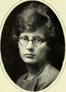 A young white woman wearing round eyeglasses and a string of pearls or beads; in an oval frame