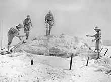 Four soldiers standing around an obscured gun position.