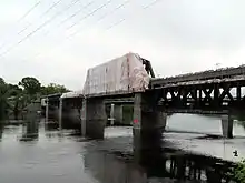 A multi-span steel railroad bridge crossing a river. One span is wrapped in plastic sheeting.