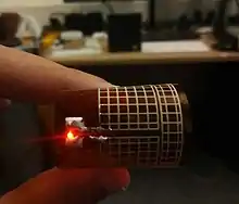A printed rectenna lighting an LED from a Powercast 915 MHz transmitter, flexible meshed antenna bent with a red LED light