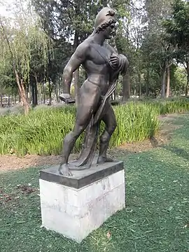Sculpture of a muscular, nude man in a fighting stance. He has a beard and a cap.