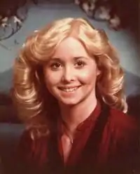 Portrait of Michelle Martinko. She has shoulder-length blonde curly hair and wears a red blouse.