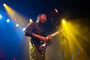Mike Kinsella with a black electric guitar singing into a microphone