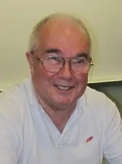 a bespectacled man with thin grey hair, laughing