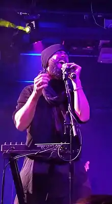 A man in a beanie stands in front of a keyboard and signs into the microphone