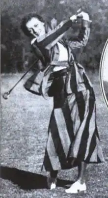 A smiling white woman in mid golf swing, wearing a long striped skirt and matching jacket