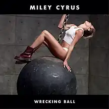 An image of Miley Cyrus sitting on a wrecking ball while holding on to a chain that is attached to it.