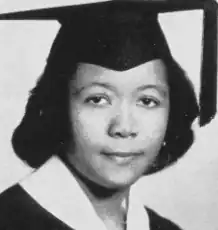 A young Black woman in a black mortarboard cap and gown