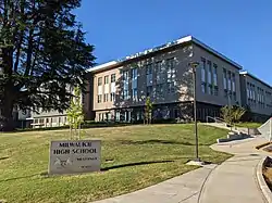 Southwest approach to the Milwaukie High School main building with the Milwaukie High sign and a tree in the foreground