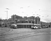 Black and white photo of corner building on a semi deserted street with round facade, sign saying Northland Greyhound, and two vertical signs reading Greyhound, surrounded by buses, Pantages Vaudeville and other buildings visible in rear