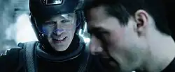 Two men, one of whom is wearing futuristic armor and helmet. A distinctive blue tint colours the image.