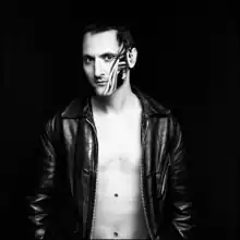 Black-and-white photo of Mirwais Ahmadzaï wearing an unzipped leather jacket with his face painted on the left side.