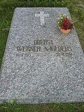 A marbled-grey stone slab, lying flat on the ground, bearing the golden inscription "Oberst Werner Mölders 18.3.1913–22.11.1944" just below the centre of the slab.