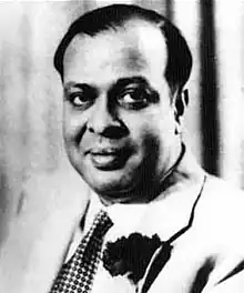 A black-and-white head and shoulder shot of a man wearing white shirt and a black tie.