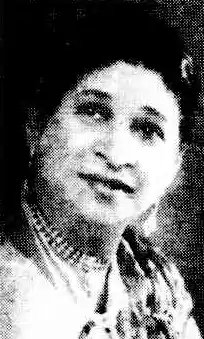 A middle-aged South Asian woman's face, from a 1950 newspaper. She is wearing beads around her neck and dangling earrings.