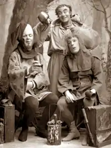 three male actors in comic medieval costume holding cups and striking exaggerated poses
