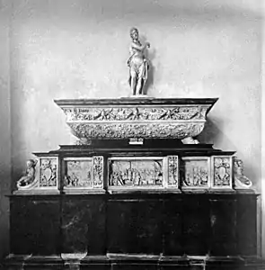 Black and white photograph of a sarcophagus topped by a statue and placed on a pedestal.