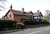 A brick and sandstone house near a road, with two gables and a dormer window, all timber framed.