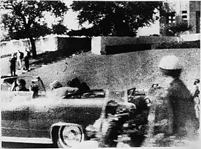 John F. Kennedy is fatally shot in the head, with Jacqueline Kennedy sitting beside him. Jacqueline can be seen turning over and looking at him at that moment.