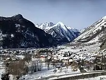 Snow covered village in valley with snow capped mountains in background taken from an elevated position on a walking trail though hills and forests