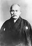 A middle-aged, mustachioed man in a kimono