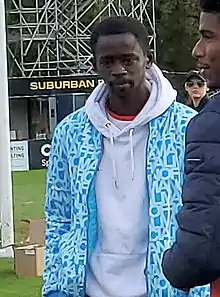 Mour Samb wearing a blue jacket over a white hoodie