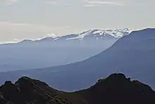 A glaciated, flat-topped, gently-sloping mountain with a much lower barren mountain in the right foreground.