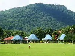Round Samoan meeting houses (fale tele) with blue painted roofs in Lepea village with Mount Vaea beyond, the burial place of Robert Louis Stevenson.
