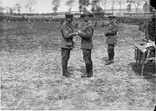 Two men in military uniform shaking hands. Groups of men are in the background.