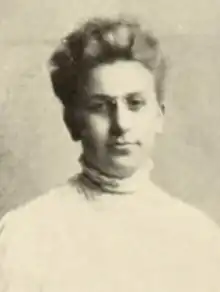 A young white woman with fair hair in an updo, wearing eyeglasses and a high-collared white dress or blouse